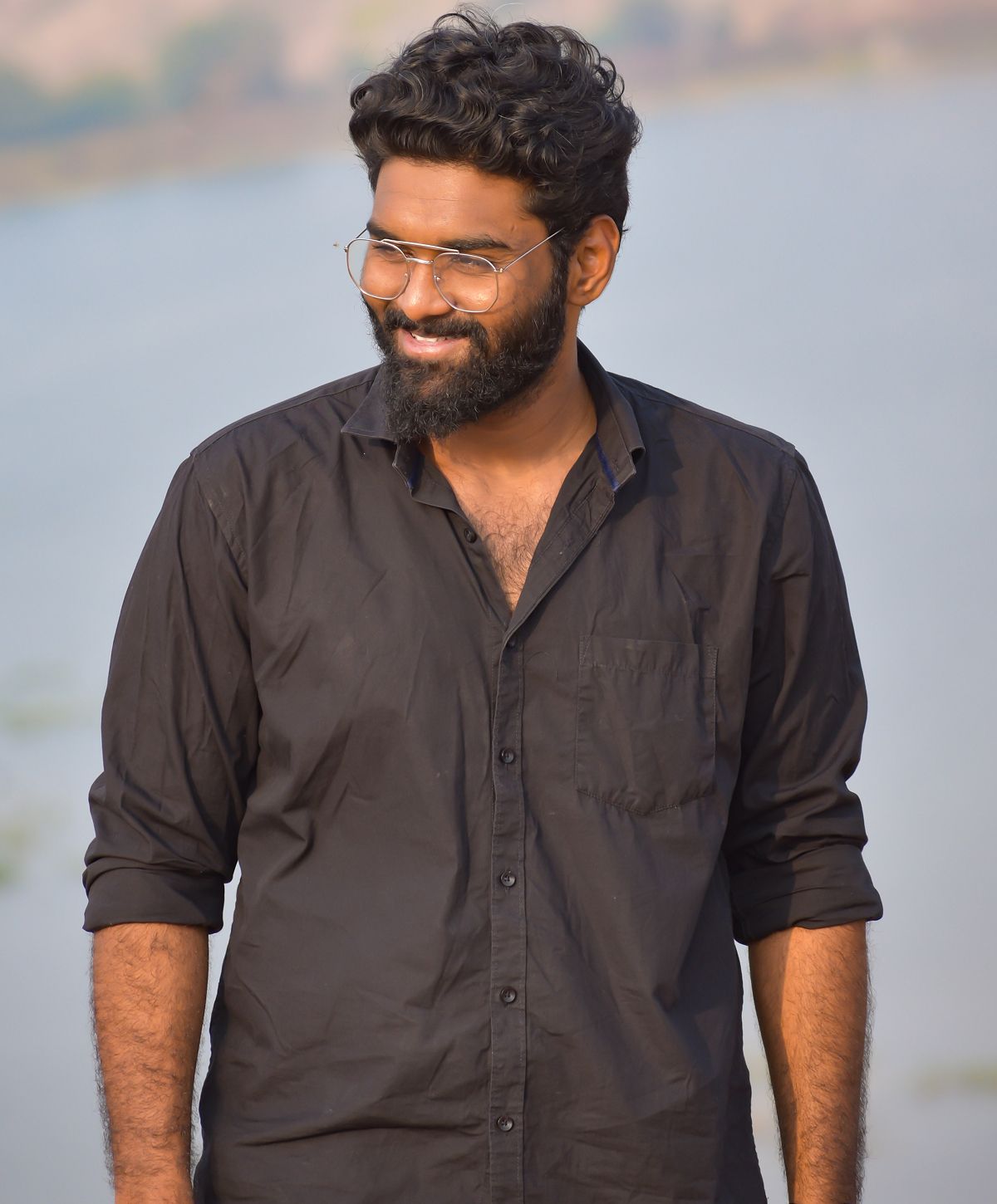 Smiling man in black shirt by water.