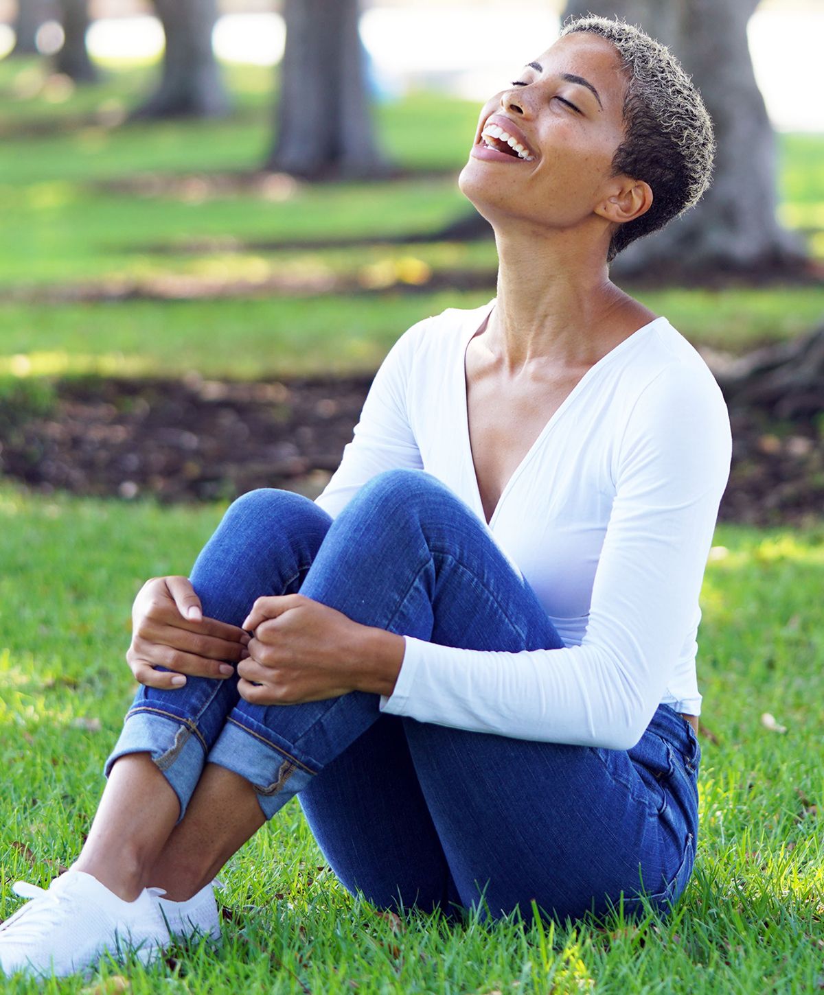 Woman sitting on grass, smiling happily outdoors.
