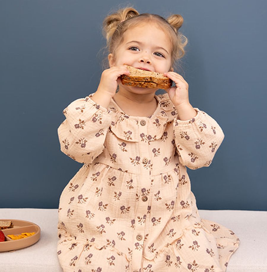 Child enjoying a sandwich, wearing floral dress.