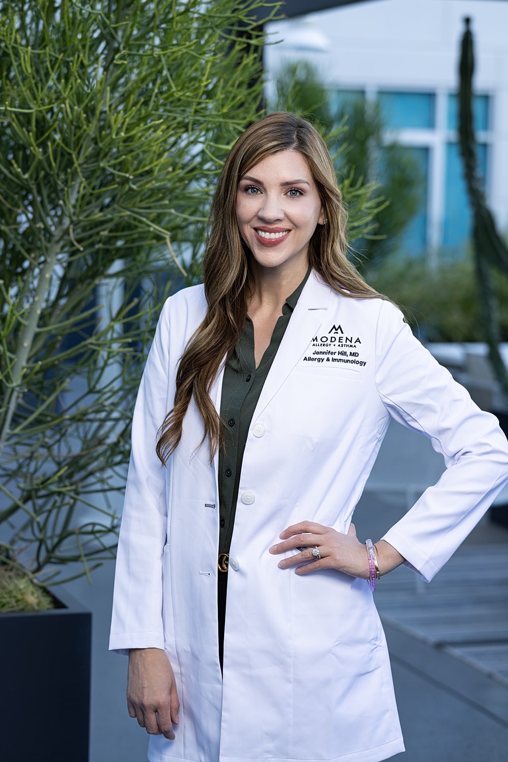 Smiling woman in a white lab coat outdoors.