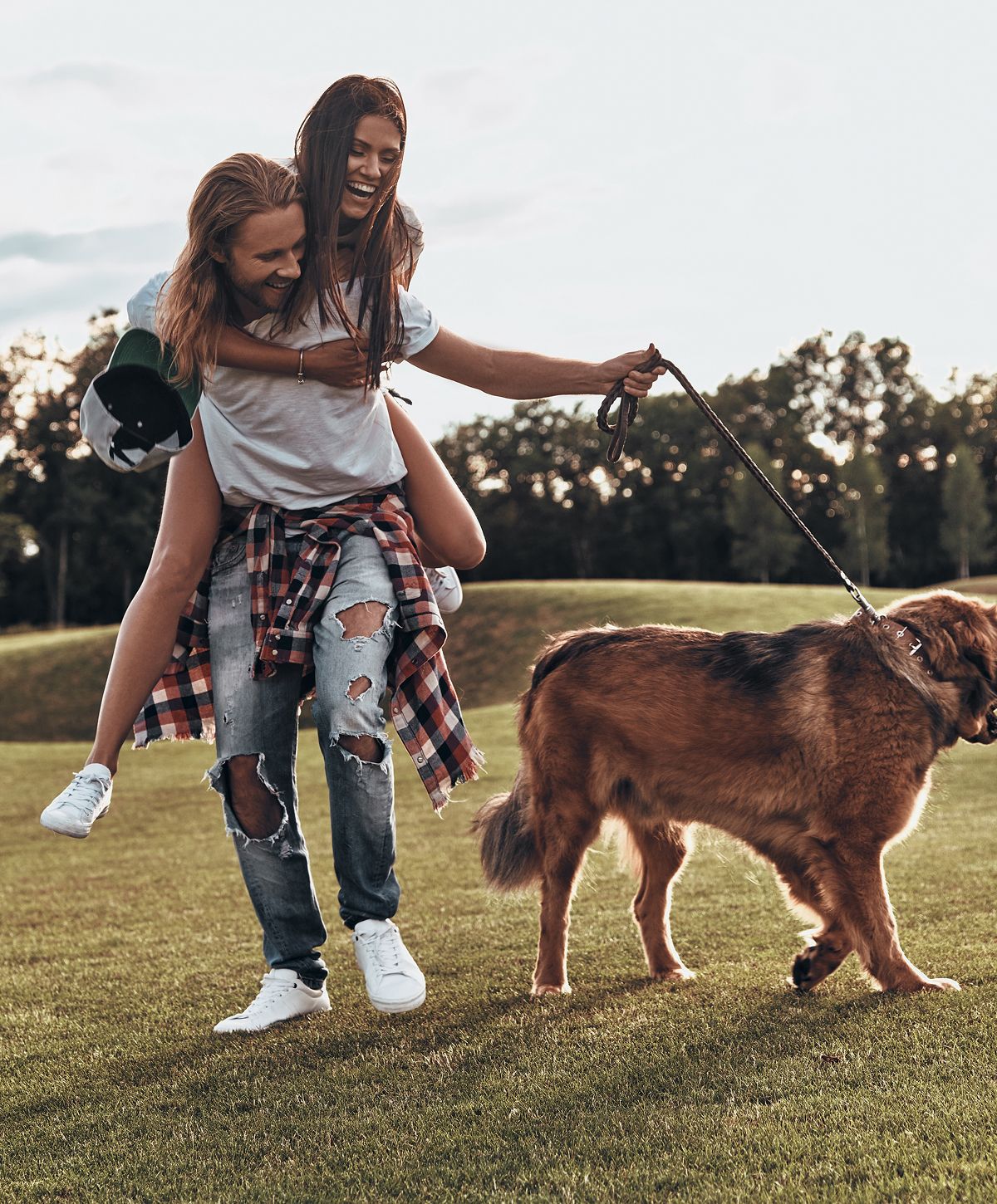 Couple playing with dog in a grassy field.