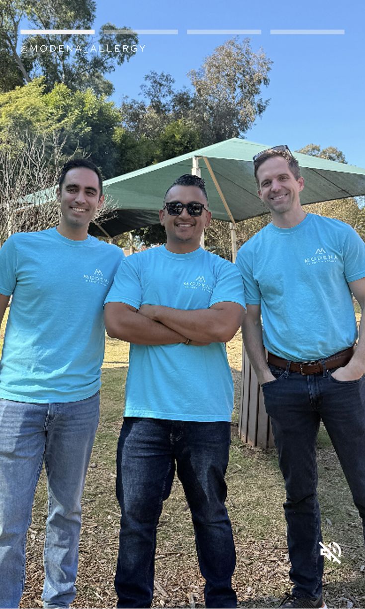 Three men in blue shirts smiling outdoors.