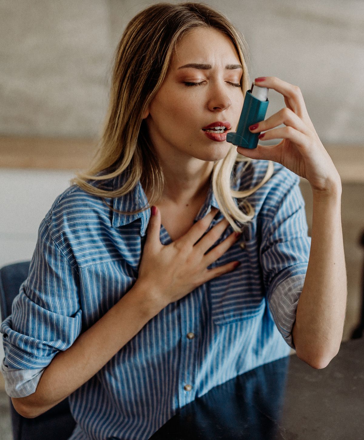 Woman using an inhaler, experiencing breathing difficulty.