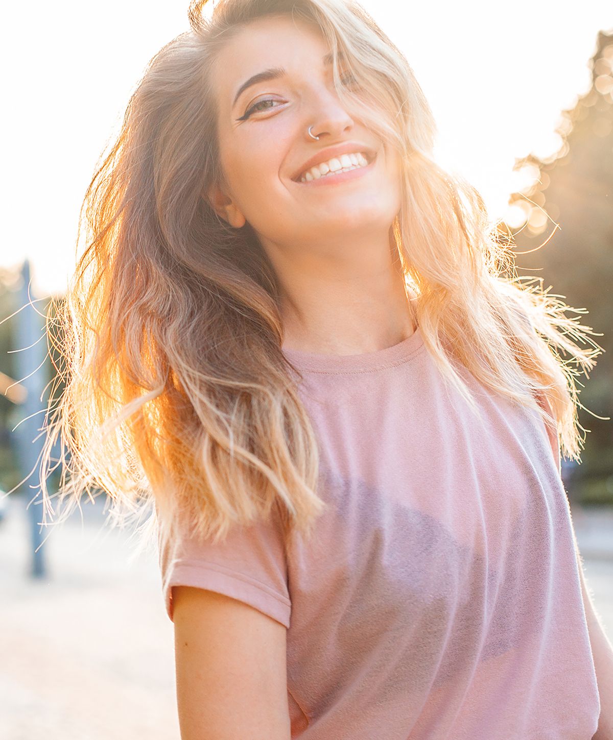 Smiling woman with sunlit, wavy hair outdoors.