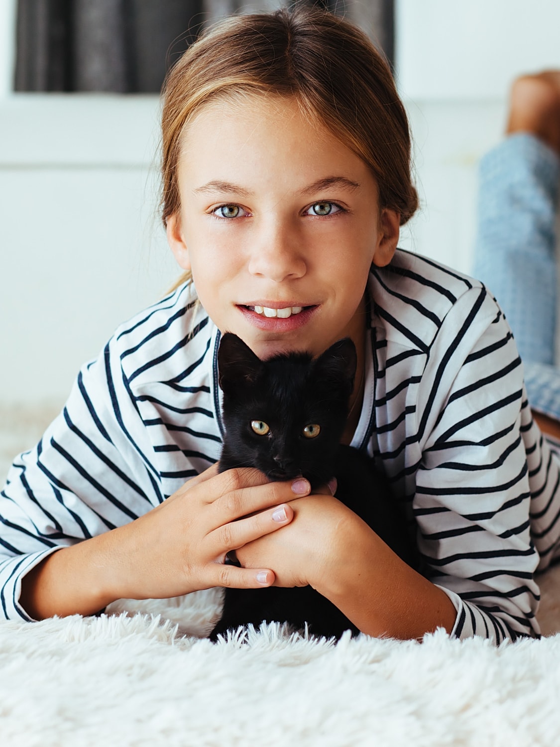 Child cuddling a black cat on a rug.