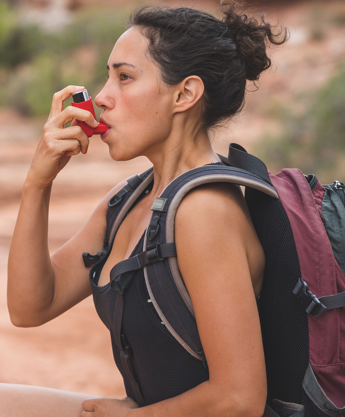 Woman using inhaler while hiking outdoors.