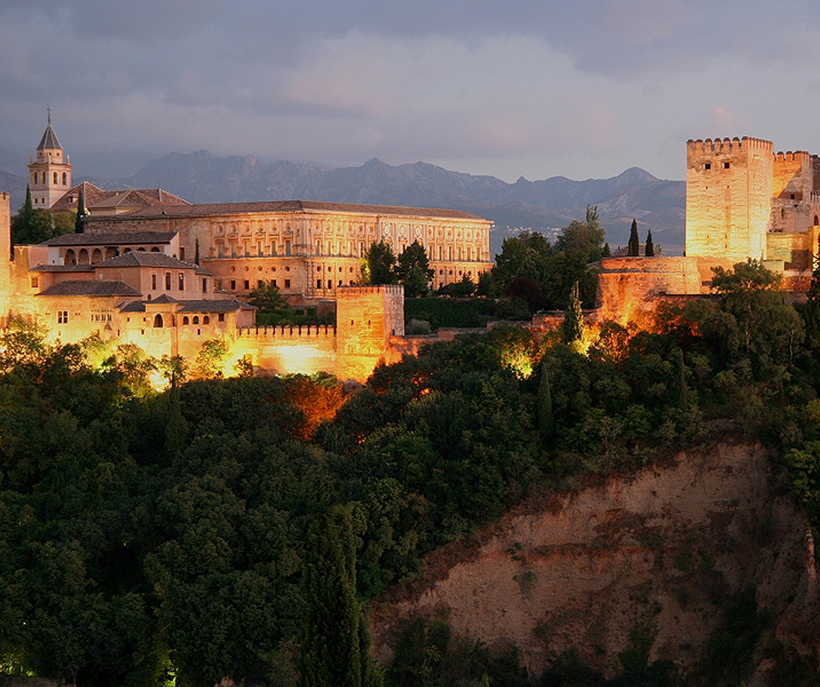 Illuminated historic fortress on a hillside at dusk.