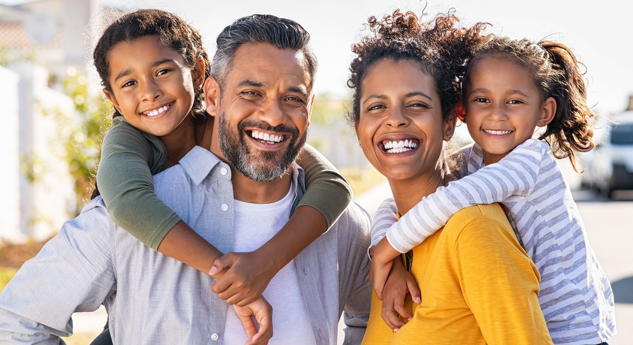 Smiling family outdoors with children on shoulders.