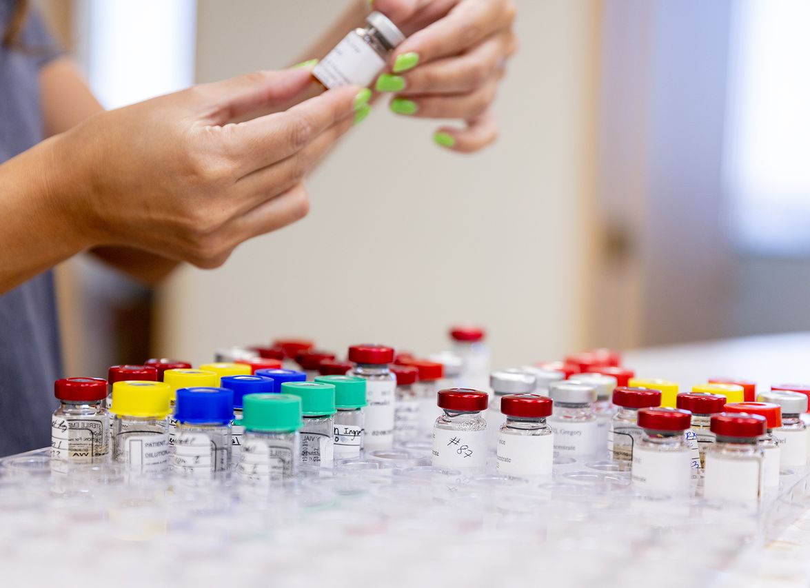 Hands holding vial among colored medicine bottles.