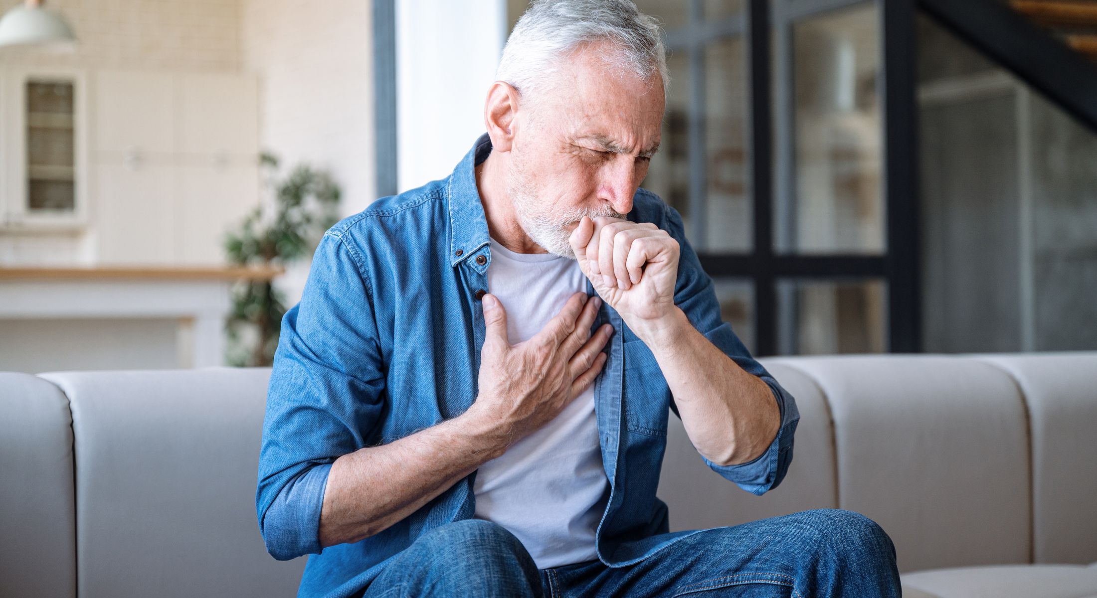 Senior man coughing at home, feeling unwell.