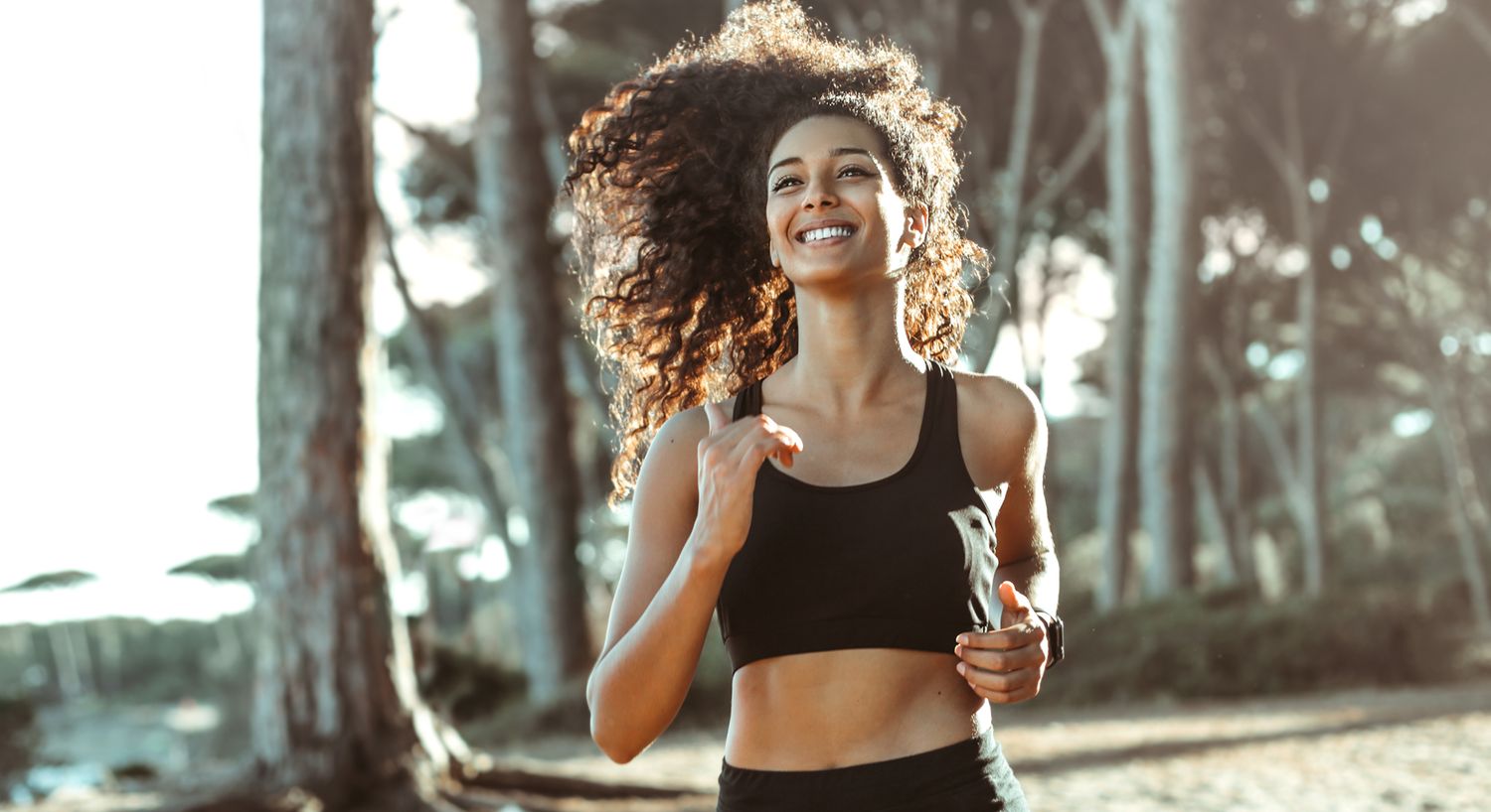 Smiling woman jogging in a sunny forest.