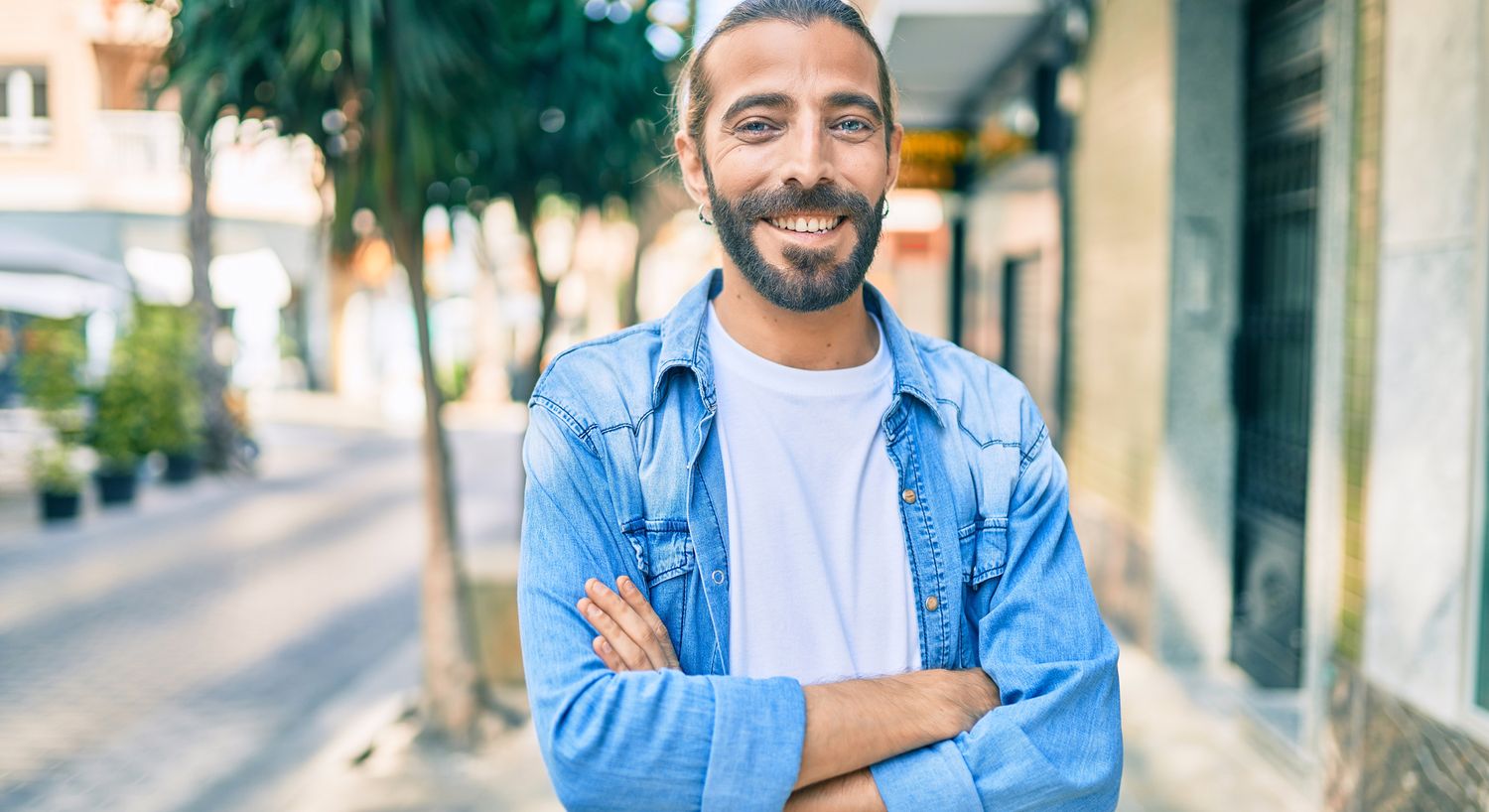 Smiling man in blue denim shirt outdoors.